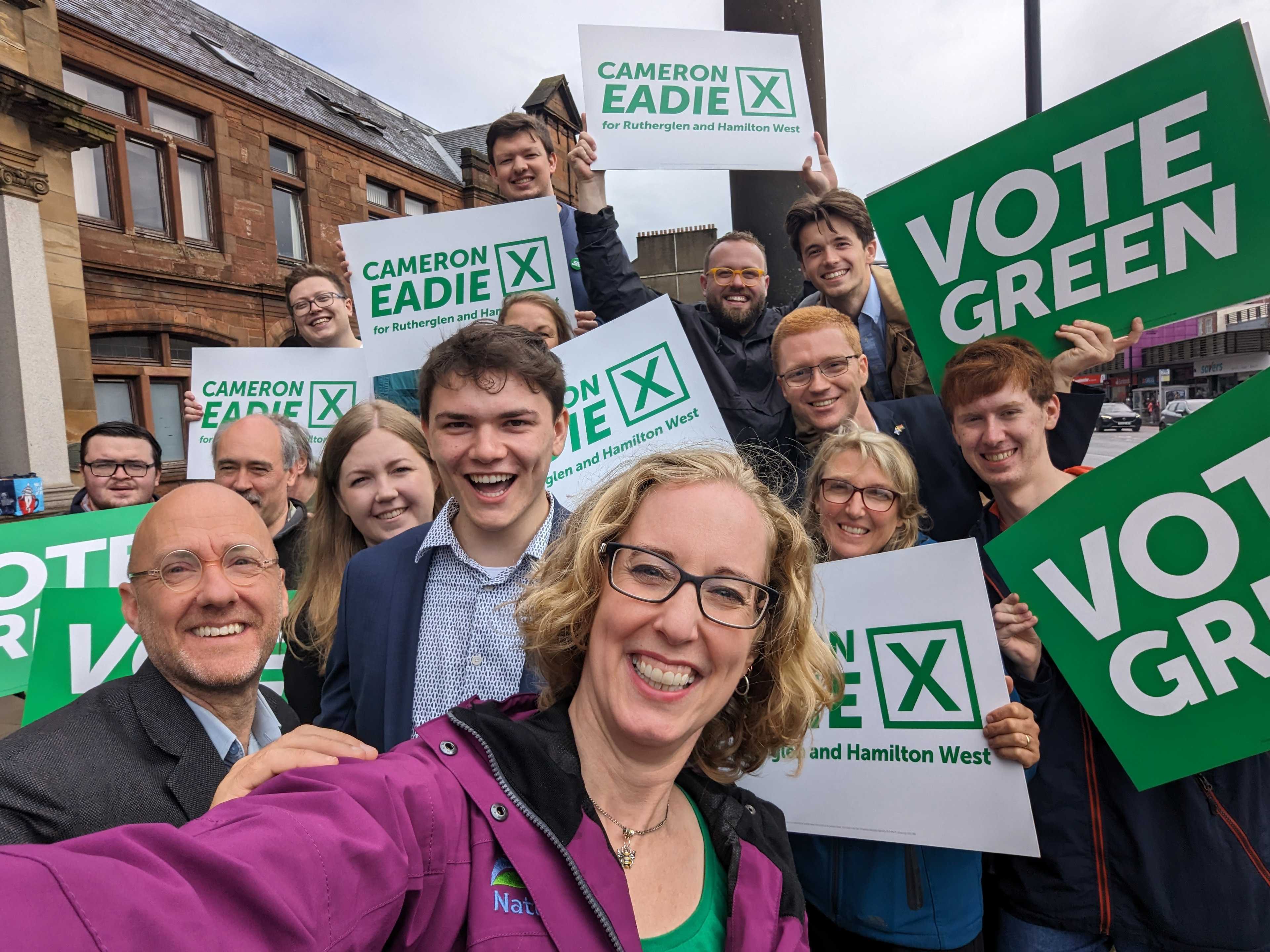 A crowd of people and MSPs with vote green placards with Cameron Eadie